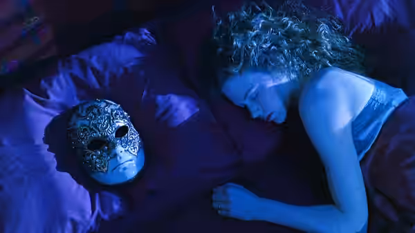 Alice Harford (Nicole Kidman) asleep beside an ornate mask on purple sheets