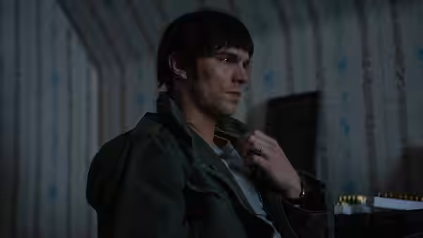 Robert Jay Mathews (Nicholas Hoult) adjusting his collar in a room