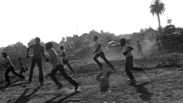 group of children running across a dusty open lot near houses