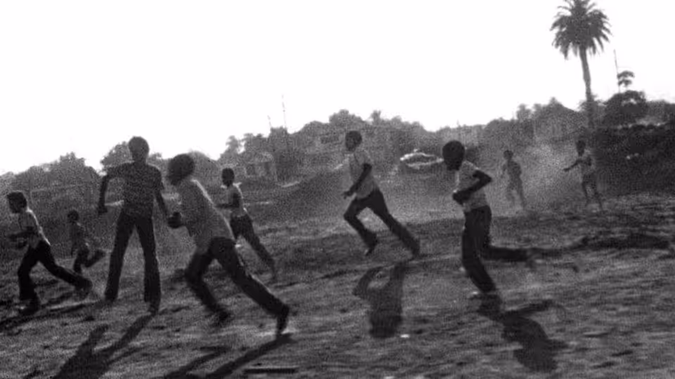 group of children running across a dusty open lot near houses