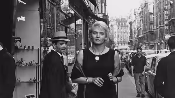 Cléo walks along a Paris street as pedestrians and cars pass behind her