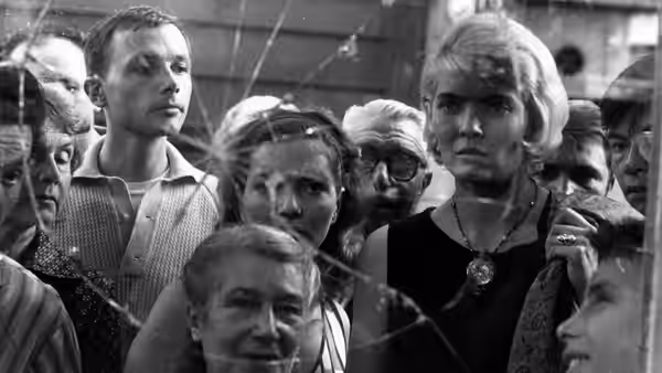 Cléo stands among a crowded group of people, staring ahead
