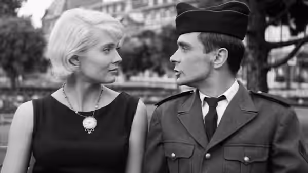 Cléo and Antoine sit side by side outdoors, looking at each other