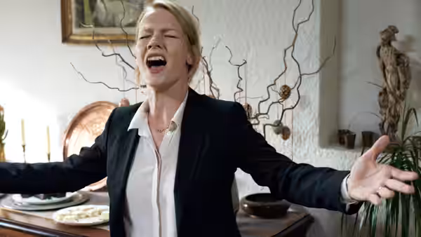 Ines (Sandra Hüller) with arms outstretched and mouth open in a dining room