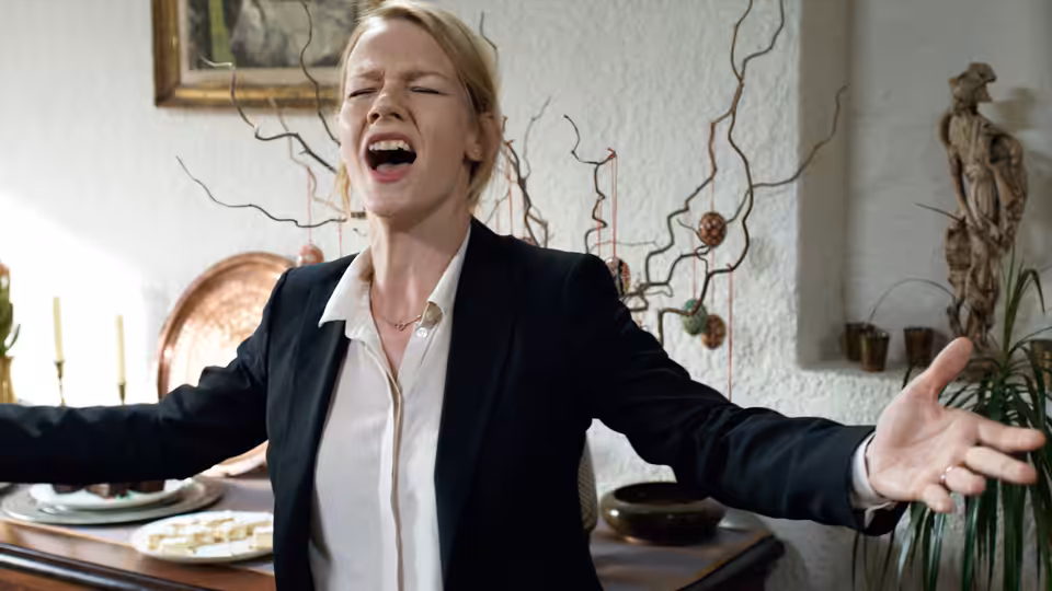 Ines (Sandra Hüller) with arms outstretched and mouth open in a dining room