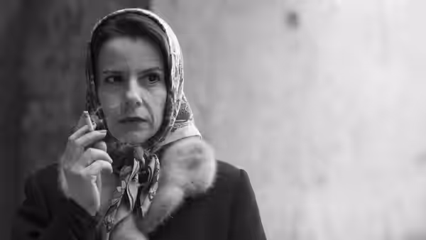 A woman in a headscarf holds a cigarette to her lips against a wall