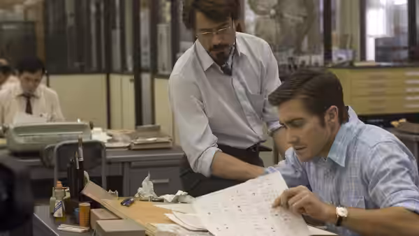 David Toschi (Mark Ruffalo) leans over Robert Graysmith (Jake Gyllenhaal) at a desk