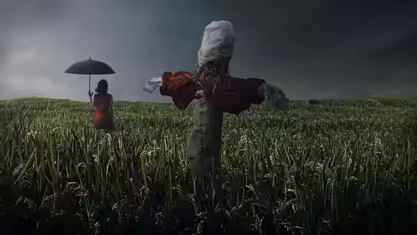 A woman in a red dress holding an umbrella near a scarecrow in a field