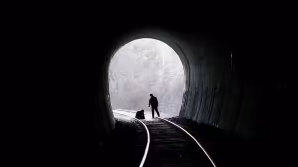 A silhouetted figure standing on railway tracks inside a dark tunnel