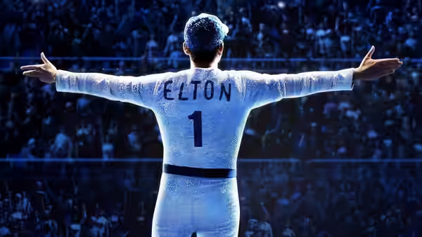 Elton John (Taron Egerton) standing with arms outstretched before a stadium crowd