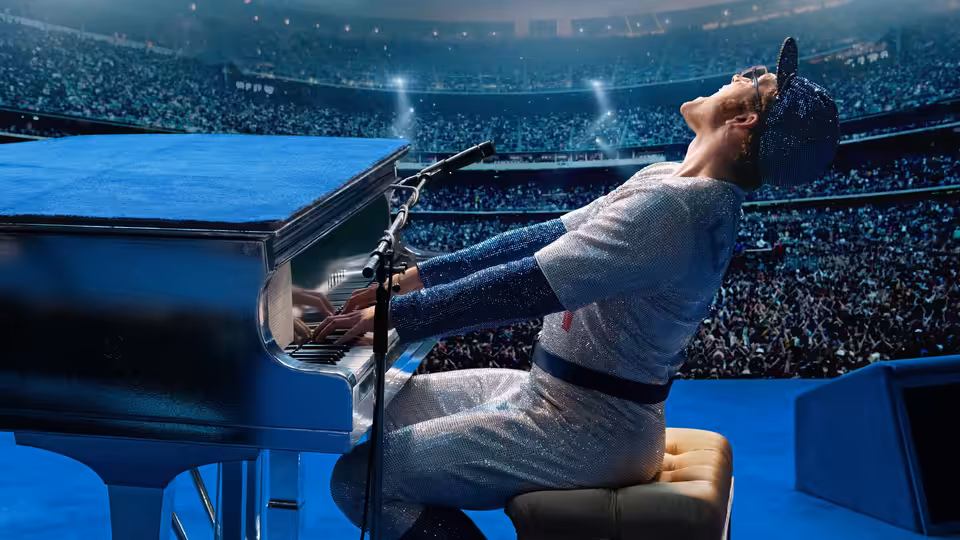 Elton John (Taron Egerton) playing piano on stage in a packed stadium